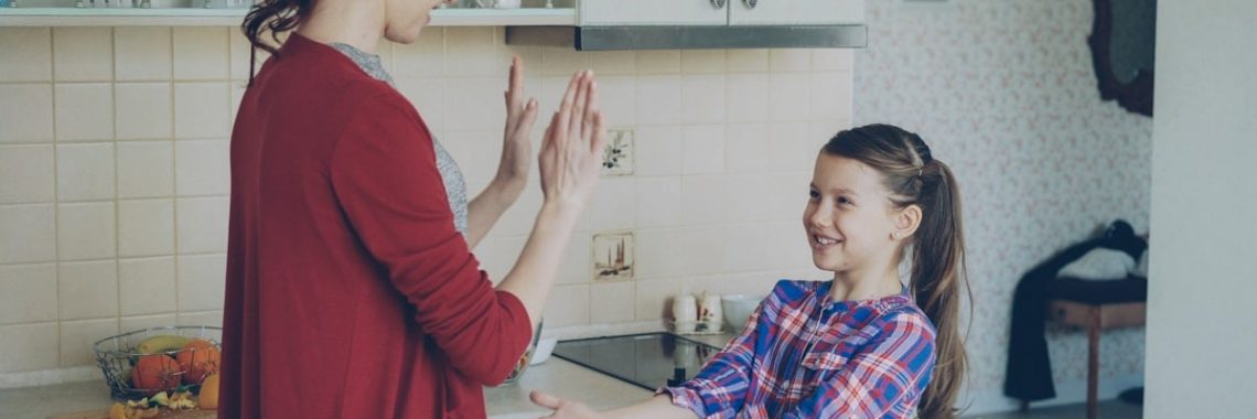 Happy young mother and cute funny daughter playing clapping hands game and have fun while cooking in kitchen at home. Family, cooking and people concept
